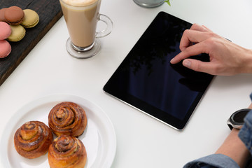 Woman with smartwatch using tablet in coffee shop. Coffee and pastry, macaroons on white table. Freelance working