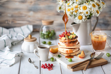 Cornmeal pancakes with salted caramel served with berries and fruits on a white wooden background.