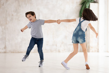 Canvas Print - Excited funny kids siblings holding hands spinning playing at home