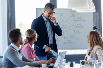 Wall Mural - Handsome businessman clearing his throat while explaining a project to his colleagues on coworking place.