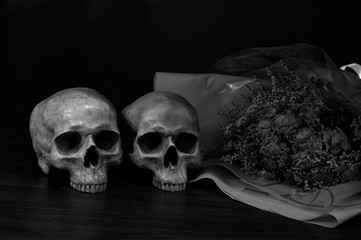 Dry bouquet flower and old two skulls on dark wooden floor in dim light room