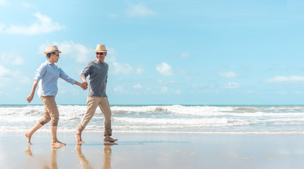 Wall Mural - Happy senior man and woman couple dancing, holding hands & splashing in sea water on a deserted tropical beach with bright clear blue sky