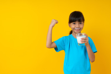 Happy Thai kid holding glass of milk isolated, young Asian girl drinking milk for strong health on yellow background