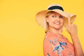 Wall Mural - Beautiful smiling and happy cute senior woman in colorful clothes is posing on yellow background. Holidays and vacation. Summer mood