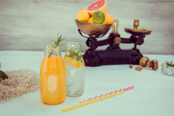 Two bottles with homemade lemonade and orange fresh juice with mint and ice on the white wooden background with fresh citrus in vintage scale and some friuts around. Healthy Summer drinks.