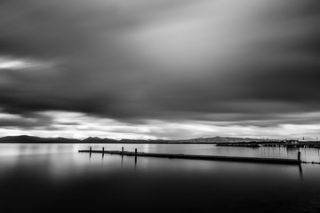 Long exposure view of a pier on a lake, with moving clouds and still water