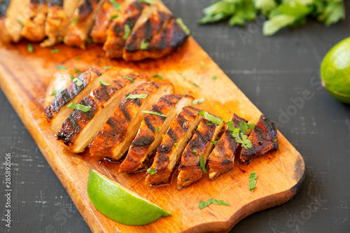 Fotomural Grilled chipotle chicken breast on a rustic wooden board on a black surface, side view