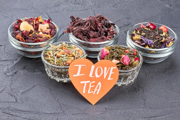 I love tea composition with assorted teas. Five glass bowls with dried tea and card with inscription I love tea.