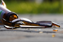Bottle Of Beer, Soda Or Drugs From Dark Glass Is Broken. Shattered Beer Bottle On Ground In Sunset Light. Fragments Of Glass On Asphalt. Texture, Background, Wallpaper.