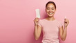 © WHstudio Leushin N - Happy satisfied Korean woman holds different types of feminine hygiene products during menstrual cycle, sanitary pad in one hand and cotton tampon in other, stands over pink wall with empty space