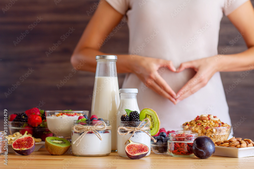 Female make shape of heart with her hands. Light summer breakfast with organic yogurts, fruits, berries and nuts. Nutrition that promotes good digestion and functioning of gastrointestinal tract. - obrazy, fototapety, plakaty 