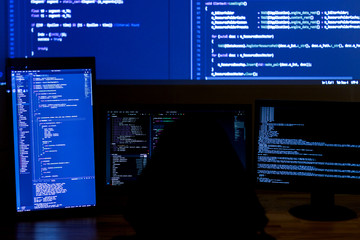 Wall Mural - back view of man in black hood is hacking password. programmer is writing malware on multiple screen