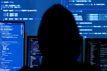 Wall Mural - back view of man in black hood is hacking password. programmer is writing malware on multiple screen