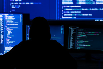 Wall Mural - back view of man in black hood is hacking password. programmer is writing malware on multiple screen