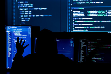 Wall Mural - back view of man in black hood is hacking password. programmer is writing malware on multiple screen