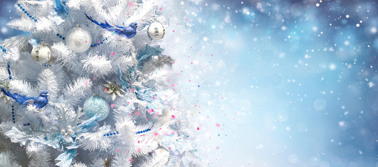 Wall Mural - White Christmas tree decorated with silver Christmas balls and beautiful blue bird good luck on sparkling background blue evening sky with falling snow flakes with beautiful bokeh, copy space.