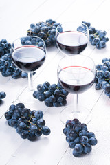 Canvas Print - three glasses of red wine and blue grapes on white wooden table background