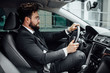 © Тарас Нагирняк - Handsome young bearded driver in full suit with fastening seat belt driving a car.