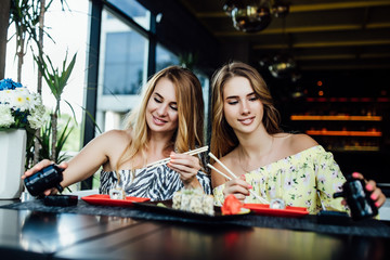 Lunch at a Chinese restaurant on the summer terrace. Mom and her young beautiful daughter eat sushi with chinese sticks. Lifestyle.