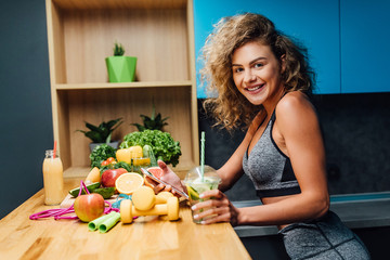 Wall Mural - Young woman wearing  top enjoying healthy breakfast, eating fruits, smiling, home kitchen time. Use phone for count calories.