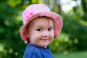 Wall Mural - Closeup of adorable fair smiling toddler girl wearing a pink straw hat looking sideways with cheeky expression