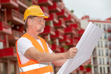 surprised worker in his 50s with helmet standing outside and holding a plan