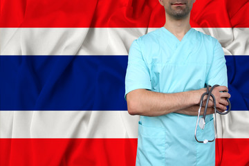 male doctor in uniform professional clothes with a stethoscope stands against the background of the national flag, the concept of the country's health and medical insurance, close-up, copy space