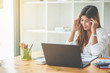 © Pissanu - Asian girl with headache while working on laptop in her office
