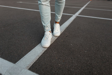 Sticker - Trendy young man in vintage white leather sneakers in fashionable blue denim pants. Stylish men's summer shoes. Casual design. Close-up of male legs.