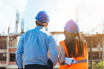 Asian man civil engineer and woman architect wearing blue safety helmet meeting at contruction site.