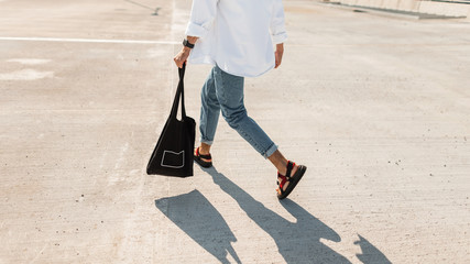 Wall Mural - Young man in fashionable summer clothes in stylish red sandals with a black vintage bag runs down the street. Close-up male legs. Trendy mens clothing. Stylish look.