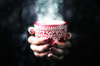 Close up of female hands holding red mug with hot drink on black background