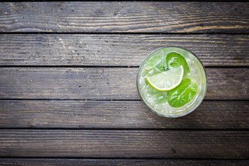 Refreshing mint cocktail mojito with rum and lime, cold drink or beverage with ice on dark wooden background, top view