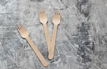 Many eco-friendly wooden forks on gray concrete background.