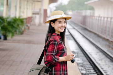 Young beautiful female travel photographer enjoys taking photo during her trip at railway station. Asian woman travel with camera having fun making pictures while waiting for train.