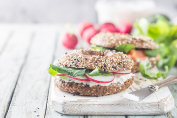 Wall Mural - Bagels with cream cheese avocado, fish, arugula and radish on old wooden table. Healthy breakfast food.