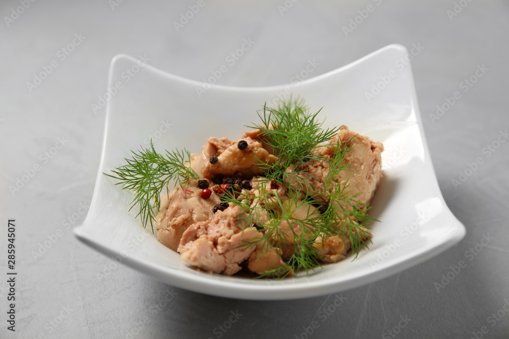 Plate with tasty canned cod liver on grey table