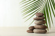 Stack of spa stones and palm leaf on table against white background, space for text