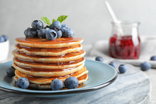 Plate Of Delicious Pancakes With Fresh Blueberries And Syrup On Grey Table Against Light Background