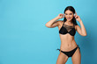 © New Africa - Beautiful young woman in black bikini with headphones on light blue background. Space for text