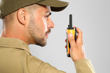 Wall Mural - Male security guard in uniform using portable radio transmitter on grey background, closeup