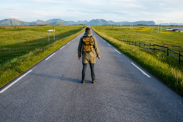 Wall Mural - Man with backpack walking on an empty road. Amazing landscape, mountain and ocean. Scenic view. New way. Enjoy the moment, relaxation. Wanderlust. Travel, adventure, lifestyle. Explore North Norway