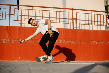 Wall Mural - Stylish young guy dressed in jeans and white t-shirt is dancing brakedance in the street against a painted concrete wall in the sunny day