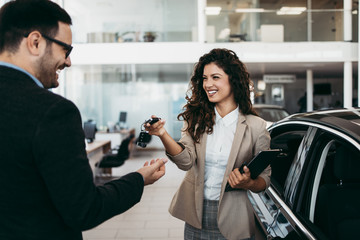 Happy middle age businessman buying new and luxury car. Beautiful female dealer gives him car keys.