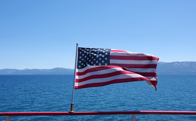 Close up view of the US flag on the stern of a steamer on a lake with mountains in background and blue sky above