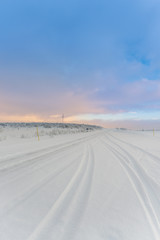 Wall Mural - tire tracks on snow covered road in an arctic landscape under a cloudy evening sky above the arctic 