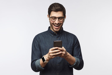 Wall Mural - Young man laughing as he is looking at phone, isolated on gray background