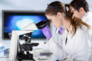 Poster - Life scientists researching in laboratory. Attractive female young scientist and her doctoral supervisor microscoping in their working environment. Healthcare and biotechnology.