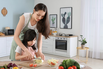 Wall Mural - Mother with cute daughter preparing vegetable salad in kitchen