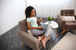 © Pixel-Shot - Beautiful African-American woman with laptop and mobile phone sitting in armchair at home
